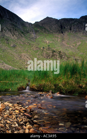 A stream that enters Llyn Idwal with the Glyders mountain range and Devils Kitchen in the background under cloud shadow, North Wales, UK Stock Photo