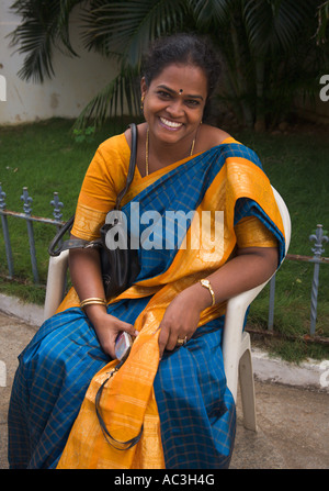 Indian lady seated dressed in blue and gold sari holding mobile phone smiles at the camera, Chennai, India Stock Photo