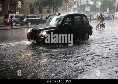 A taxi cab and cyclist make their way along a flooded Marylebone Road in London, during a summer rain storm Stock Photo