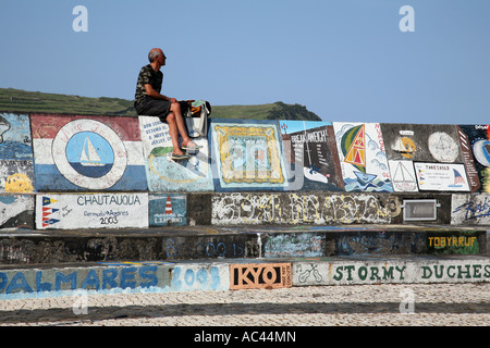 A tourist sits on the breakwater which is covered with paintings, Horta Harbour, Faial, The Azores Stock Photo