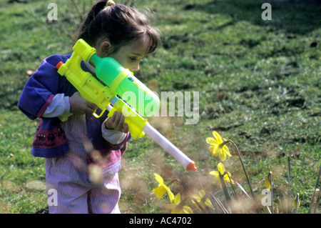 3 year old girl watering flowers with plastic water cannon gun Stock Photo