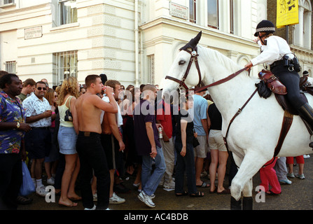 Large crowd be directed and controlled by a mounted police officer in a side street at Notting Hill Gate carnival.