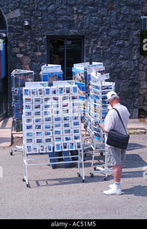 Sunny day beside the coast road from Ajaccio smart tourist man outside souvenir shop viewing picture postcards on display panels Corsica France Stock Photo