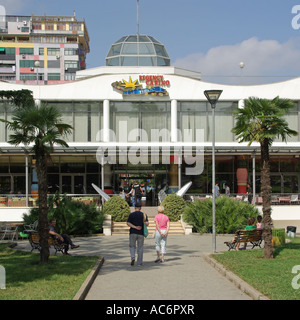 Back view of couple of people walking along path in park towards sign & entrance to the Tirana Regency Casino building in Tirana Republic of Albania Stock Photo