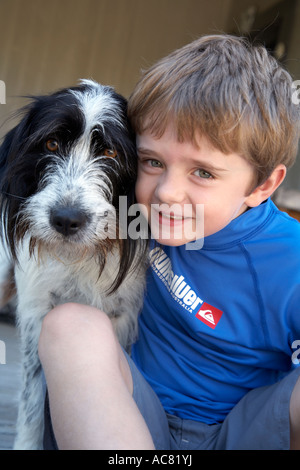 boy 7 sitting with pet dog on deck Stock Photo