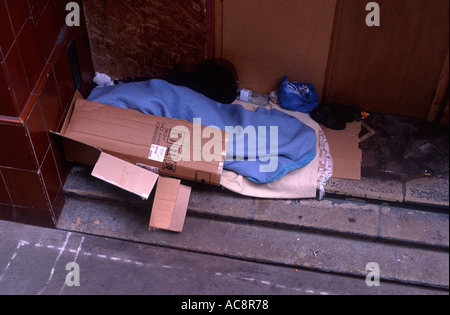 Homeless person sleeping under blankets and cardboard beside a building near St Paul's, City of London, England Stock Photo