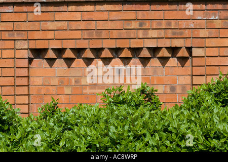 Corbelling in brickwork providing relief pattern on red brick wall contrasting with green shrubs below Tewkesbury UK Stock Photo