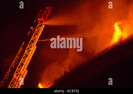 Firefighters / Firemen fighting Blazing Fire and Flames in a Burning Building with Water Hose from an Aerial Extension Ladder Stock Photo