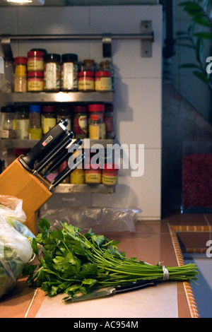 a bunch of parsley waits to be chopped on a chopping board, with a spice rack in the background and knives visible Stock Photo