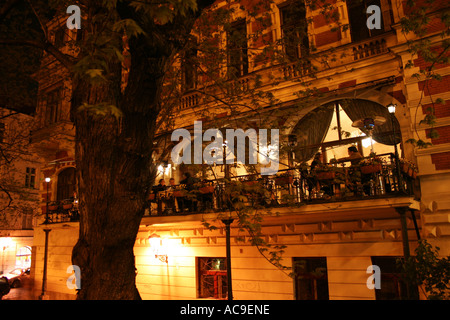 Outdoor restaurant on a charming balcony of a historic building in Prague, illuminated at night, with people dining and enjoying the ambiance. Stock Photo