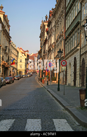Nerudova Street in the early morning in Prague, lined with historic buildings and street lamps, with cars parked along the cobblestone road. Stock Photo