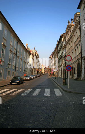 Nerudova Street in the early morning in Prague, lined with historic buildings and street lamps, with cars parked along the cobblestone road. Stock Photo