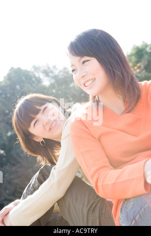 Two young women sitting on lawn smiling Stock Photo