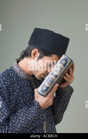 Side profile of a young man holding the Koran against his forehead Stock Photo
