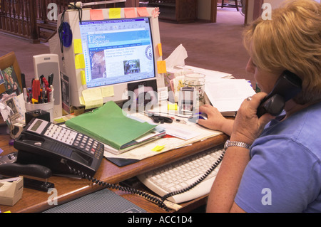 Office worker on phone while using computer mouse Stock Photo