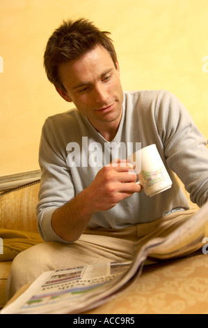 man reading a paper while drinking a mug of tea or coffee Stock Photo