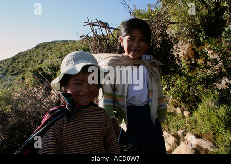 Small girls carrying woodfire walking down path on Isla del Sol, Sun Island, Lake Titicaca, Bolivia Stock Photo