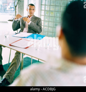 Two men conversing sitting by a table in an office environment. Stock Photo