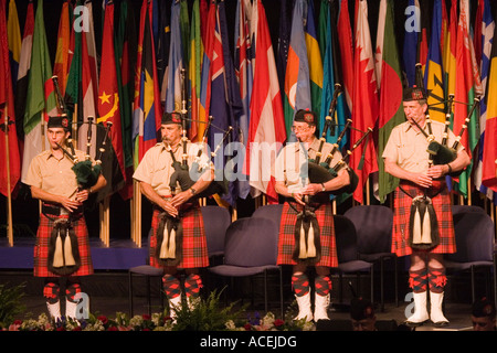 Four men in Scottish uniforms playing bagpipes in a bagpipe band on a stage with international flags Stock Photo