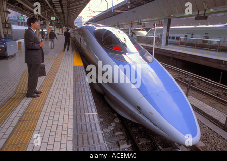 Sleek shinkansen bullet train called Nozomi stops momentarily at Tokyo Station while a businessman waits Stock Photo