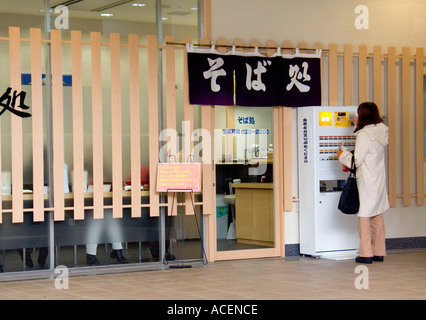 Woman in a train station purchasing a lunch meal ticket for a bowl of soup from a vending machine
