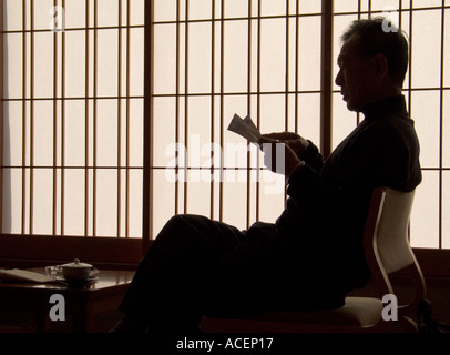 Silhouette of man in front of shoji screen relaxing reading a newspaper and having a cup of Japanese tea Stock Photo