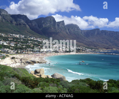 A wave washing up on the rocks at Camps Bay against the backdrop of the twelve apostles and distant bathers on the beach. Stock Photo