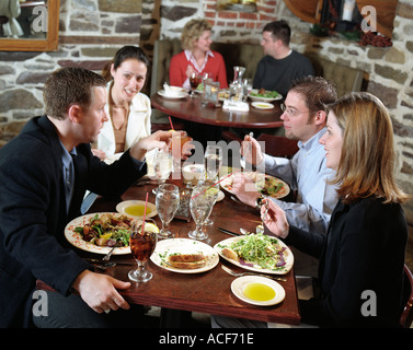 Two couples having a conversation while dining together at a restaurant Another couple sits in a corner booth behind them Stock Photo