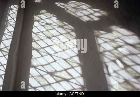 The projection of perpendicular diamond leaded windows with uneven handmade glass onto a white painted wall Stock Photo