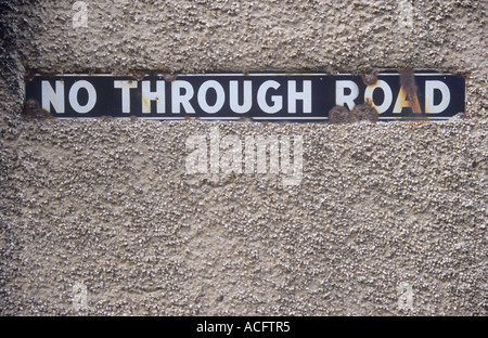 Close up of chipped rusting enamel blue and white sign stating No through road and set in pinky beige pebbledash wall Stock Photo