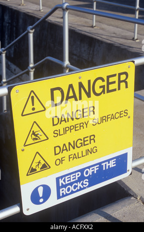 Close up of sunlit sign on jetty or promenade stating Danger Slippery surfaces Danger of falling Keep off the rocks Stock Photo