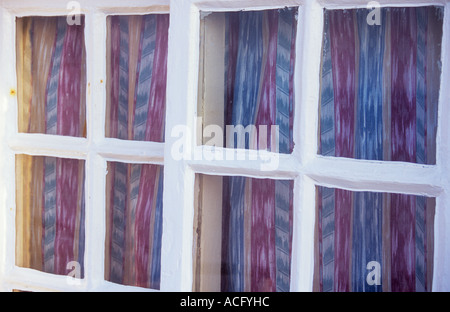 Close up detail of a beach hut or summerhouse or cottage with white painted window frames and red and blue striped curtains Stock Photo