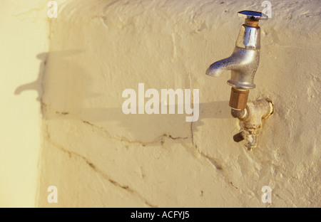 Close up of a pushdown outside tap fixed to a painted rendered cream wall and casting a shadow into a corner Stock Photo