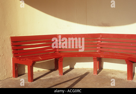 Detail of a red bench seat in a modernistic circular cream shelter casting an interesting curved shadow Stock Photo