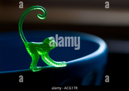 A translucent green plastic toy monkey balanced on the rim of a blue bowl. Stock Photo
