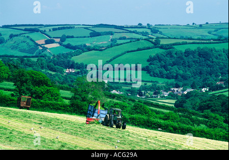 Farmer on tractor cutting grass silage hay in farm field above Winsford village in Somerset, England, UK. Summer. Stock Photo