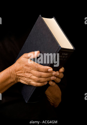 An old woman holds a bible in prayer Stock Photo