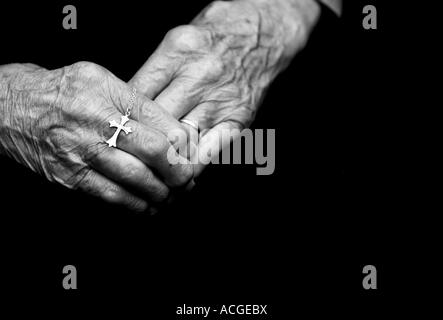One hundred year old ladies hands holding a silver cross. Black and white Stock Photo