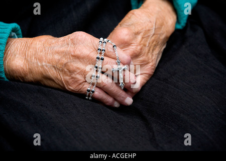 One hundred year old ladies hands holding a rosary against a dark background Stock Photo