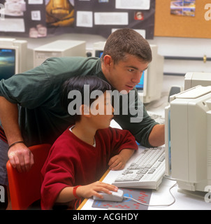Teacher and junior oriental schoolboy studying together at a computer in school classroom Stock Photo