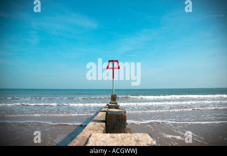 A bright red beach marker situated on a sea defence wall break. The tide is coming in with relaxing waves and blue sky Stock Photo