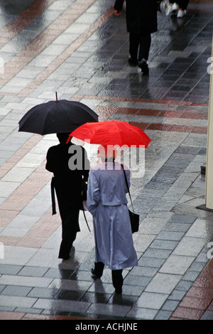 Two women walking with umbrellas in rain storm Seattle Washington USA Stock Photo