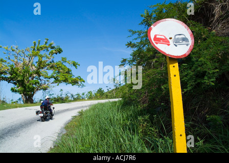 Weathered 'no overtaking' road sign and a policeman on motorbike near Trinidad, Cuba. Stock Photo