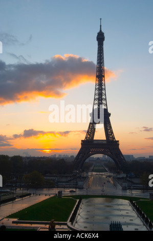 The Eiffel Tower in Paris in early morning dawn with the sun rising on the horizon, pale blue sky some white clouds and the sunlight golden yellow seen from the Place Trocadero square Paris France