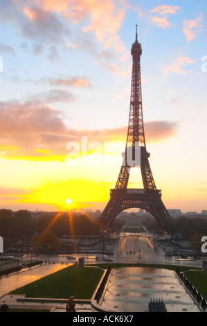 The Eiffel Tower in Paris in early morning dawn with the sun rising on the horizon, pale blue sky some white clouds and the sunlight golden yellow seen from the Place Trocadero square Paris France