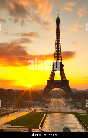 The Eiffel Tower in Paris in early morning dawn with the sun rising on the horizon, pale blue sky some white clouds and the sunlight golden yellow seen from the Place Trocadero square Paris France