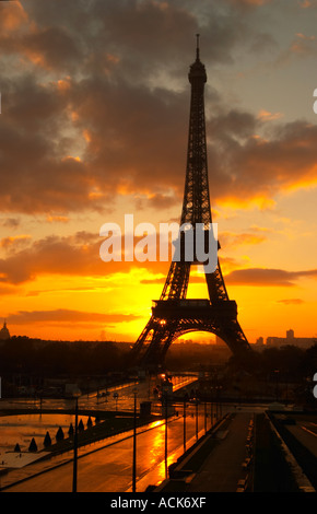 The Eiffel Tower in Paris in early morning dawn with the sun rising on the horizon, pale blue sky some white clouds and the sunlight golden yellow seen from the Place Trocadero square Paris France