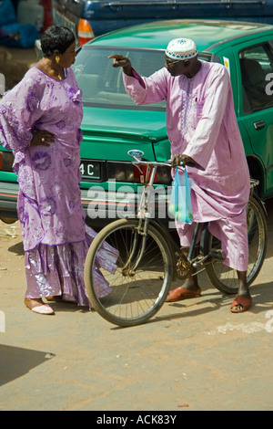 Man on bicycle and standing woman in traditional clothes have vigorous discussion in street Serekunda Market The Gambia Stock Photo