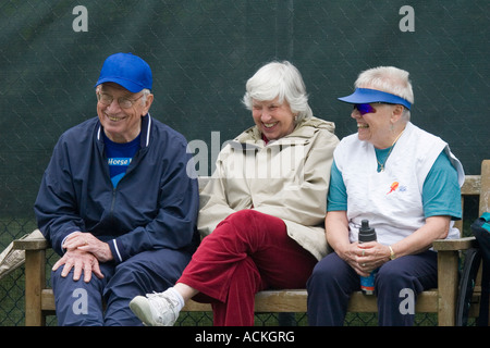 Three gray haired retired seniors, two women and one man, sitting on a bench and sharing a hearty laugh Stock Photo
