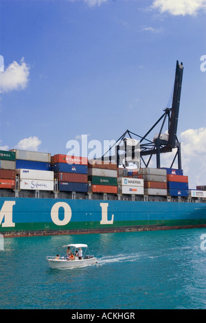 Small pleasure boat driving by a container ship loaded with cargo docked beside a giant crane at Port of Miami Florida Stock Photo